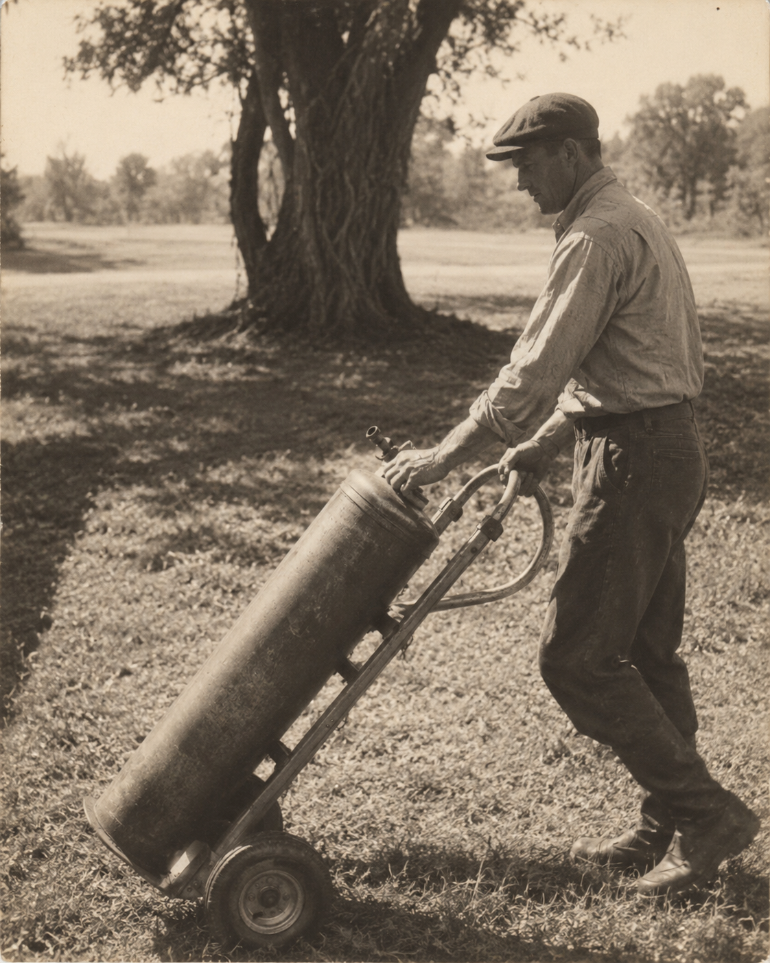 A man wheels a portable water softening exchange tank, 1930s